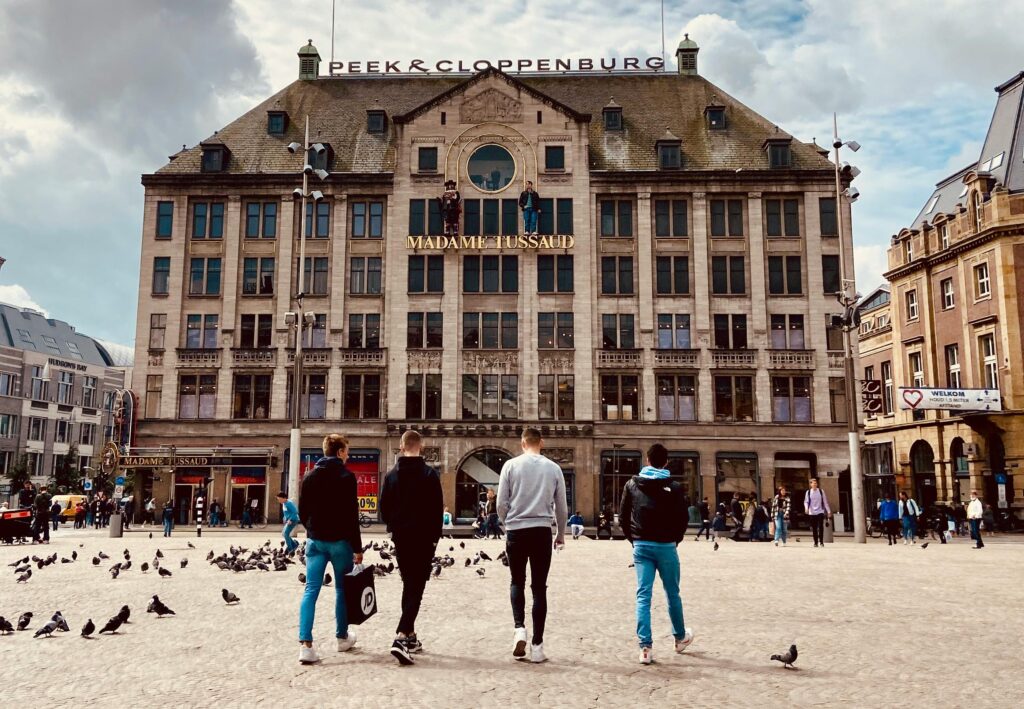 People walking in front of Madame Tussauds in Amsterdam with pigeons and iconic architecture.